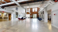 Located at 50 S Highland Ave in West York, PA, this impressive adaptive reuse space masterfully preserves the character of its industrial origins while offering a range of modern functional areas. The building's defining architectural feature is its exposed red brick walls, which appear throughout virtually every room, complemented by soaring ceilings, structural steel columns, and polished concrete floors that reflect natural light pouring in through large, arched and grid-paned windows.

The grand main hall serves as the heart of the facility, offering a dramatic double-height volume with an open mezzanine level above, visible steel beams, and generous seating areas. A bold red barn-style sliding door adds a striking design accent to the entry corridor. The polished concrete floors carry through the hallways and common spaces, lending a cohesive industrial aesthetic throughout.

A well-equipped fitness center features treadmills, ellipticals, and wall-mounted displays, bathed in natural light from original-style windows set against exposed brick. Flexible rooms with polished floors and corrugated metal wainscoting offer versatile utility. Additional gathering rooms, including a bright lounge with children's furnishings and a casual meeting area with a round table, round out this dynamic, community-oriented space.