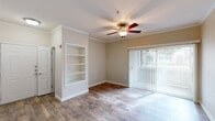 This single-floor, one-bedroom residence offers a thoughtfully organized layout that maximizes every square foot. The open-plan kitchen and living room serves as the heart of the home, featuring warm wood-look flooring, crown molding, and a ceiling fan that add a polished, cohesive feel. The living area is highlighted by a built-in shelving unit, a large sliding glass door with vertical blinds that invites natural light and outdoor views, and direct access to the kitchen. The galley-style kitchen is well-equipped with white cabinetry, granite-style countertops, stainless steel appliances including an electric range, microwave, and dishwasher, and a double basin sink. The bedroom is carpeted for comfort, features its own ceiling fan, and receives natural light through a generous window overlooking a green outdoor setting. The full bathroom includes a white vanity with dark countertop, a large mirror with overhead lighting, and a full soaking tub with shower. A dedicated laundry area houses a full-size washer and dryer. A hallway and closet complete the layout, providing convenient storage. Warm neutral tones throughout create a welcoming, move-in-ready ambiance.