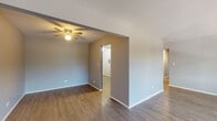 Located at 563 Deere Park Circle in Bartlett, Illinois, this single-floor residence offers a straightforward and functional layout. The open living and dining areas are finished with wood-style laminate flooring throughout, lending a cohesive, clean aesthetic. A ceiling fan with a built-in light fixture is positioned in the main living area, and the space connects naturally to adjacent rooms through open doorways, creating an easy flow. A large picture window in one of the main rooms draws in generous natural light and frames views of mature trees outside, further enhancing the bright and airy feel. Baseboard heating units run along the walls in multiple rooms, providing consistent warmth throughout.

The kitchen is equipped with gray cabinetry featuring contemporary hardware, a white countertop with a stainless steel double sink, a black gas range with overhead ventilation, and a classic white tile backsplash. The bedrooms are carpeted for comfort and each includes a built-in closet with shelving and a rod for storage. The bathroom features a full tub and shower combination with white tile surround and a curved shower curtain rod. Throughout the unit, neutral gray walls and white trim create a clean, move-in ready environment.