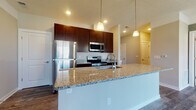 Located at 1733 Bellmeadow Dr in Lancaster, Ohio, this single-floor home offers a thoughtfully designed open-concept layout that seamlessly connects the living and kitchen areas. The kitchen is a standout feature, showcasing rich dark-wood cabinetry, granite countertops, and a full suite of stainless steel appliances including a refrigerator, range, and built-in microwave. A spacious kitchen island with matching granite provides additional workspace and casual seating, illuminated by elegant pendant lighting overhead. Durable hardwood-style flooring flows throughout the main living areas, lending warmth and a cohesive aesthetic to the space. The living area is bright and open, benefiting from large windows and a sliding glass door dressed with vertical blinds that invite ample natural light. The bedroom features plush carpeting and a generously sized window that continues the theme of natural light. The bathroom is well-appointed with dark wood cabinetry, granite countertops, a tub-shower combination, and wood-look flooring that ties the overall design together. Neutral wall tones throughout the home create a clean, versatile backdrop suited to a variety of interior styles. Recessed lighting and pendant fixtures provide layered illumination across the main living areas.