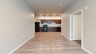 Located at 3040 Bellevue Way NE in Bellevue, Washington, this single-floor, 3-bedroom, 2-bathroom unit offers a practical and well-organized layout. The open-concept living and kitchen area features light hardwood-style flooring throughout, recessed lighting, and a kitchen equipped with rich dark cabinetry, black appliances including a gas range, refrigerator, and dishwasher, alongside a double-basin sink with light countertops. The living area is bright and connected, with a window bringing in natural light and views of surrounding greenery. A central hallway connects the main living spaces to the three bedrooms, each carpeted for comfort and painted in neutral tones. The bedrooms are well-proportioned, with sliding or standard closet doors providing generous storage. Multiple bedrooms feature windows overlooking lush, tree-lined outdoor views, adding a sense of tranquility. The unit includes five closets total, offering exceptional storage throughout. The two bathrooms are clean and functional — one featuring a full soaking tub with a shower rod and dark vanity cabinetry, and the other a simple, utilitarian design. The consistent neutral palette and practical finishes throughout the space create a cohesive, move-in ready environment well-suited for everyday living in the heart of Bellevue.