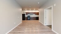 Located at 3040 Bellevue Way NE in Bellevue, Washington, this single-floor, 3-bedroom, 2-bathroom unit offers a practical and well-organized layout. The open-concept living and kitchen area features light hardwood-style flooring throughout, recessed lighting, and a kitchen equipped with rich dark cabinetry, black appliances including a gas range, refrigerator, and dishwasher, alongside a double-basin sink with light countertops. The living area is bright and connected, with a window bringing in natural light and views of surrounding greenery. A central hallway connects the main living spaces to the three bedrooms, each carpeted for comfort and painted in neutral tones. The bedrooms are well-proportioned, with sliding or standard closet doors providing generous storage. Multiple bedrooms feature windows overlooking lush, tree-lined outdoor views, adding a sense of tranquility. The unit includes five closets total, offering exceptional storage throughout. The two bathrooms are clean and functional — one featuring a full soaking tub with a shower rod and dark vanity cabinetry, and the other a simple, utilitarian design. The consistent neutral palette and practical finishes throughout the space create a cohesive, move-in ready environment well-suited for everyday living in the heart of Bellevue.