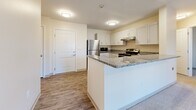 Located at 2000 NE Coronado Dr in Blue Springs, MO, this 2-bedroom, 1-bathroom unit offers a well-designed, single-floor layout. The kitchen is a standout feature, showcasing white shaker-style cabinetry, granite countertops, and a full suite of stainless steel appliances including a refrigerator, electric range, dishwasher, and built-in microwave. A peninsula with bar-style seating connects the kitchen to the open-concept living area, which is carpeted and brightened by a set of French-style doors that invite natural light. The two bedrooms are carpeted and finished with neutral tones, offering a calm and versatile environment. The primary bedroom includes a double-door closet, providing ample storage. The bathroom features a walk-in shower with a clean white surround, white cabinetry, and granite countertops consistent with the rest of the unit. A dedicated laundry room houses a full-size washer and dryer with overhead shelving for added utility. Wood-style vinyl flooring flows through the kitchen, bathroom, and laundry areas, complementing the warm, neutral color palette found throughout the entire space.