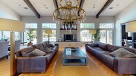 Located at 1373 Ivy Ln in Naperville, IL, this single-floor community facility offers a thoughtfully designed space that combines elegance with functionality. The centerpiece of the clubhouse is a grand lounge area distinguished by soaring vaulted ceilings adorned with dark exposed beams and a striking pair of tiered brass chandeliers with elongated pendant lights that serve as dramatic focal points. Large multi-pane windows wrap the lounge, flooding the space with abundant natural light and providing views of the surrounding outdoor area. Rich hardwood flooring runs throughout, complementing the warm, inviting atmosphere. Deep leather sofas flank a substantial wooden coffee table, arranged around a floor-to-ceiling stone fireplace that anchors the room.

Adjacent to the lounge is a stylish bar area, featuring a dark accent wall, a circular mirror, industrial-style bar seating, and a wood-topped counter — ideal for casual gatherings. The space also connects seamlessly to a well-equipped fitness center, visible through interior windows and glass-paned doors. The fitness area features rubberized flooring, cable weight machines, free weights, cardio equipment, and natural light from exterior windows. The overall design balances modern sophistication with comfortable, community-focused amenities throughout.