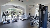 This dedicated fitness center is designed to support a comprehensive workout experience within a single, thoughtfully appointed floor. The space features soaring vaulted ceilings that lend an open, airy atmosphere, complemented by large arched windows that flood the room with abundant natural light and provide views of the surrounding greenery. A ceiling fan helps maintain comfortable air circulation throughout the space during intense workouts.

The facility is well-stocked with a variety of cardio equipment, including treadmills and an elliptical cross-trainer, each equipped with personal display consoles. Strength training needs are addressed with a multi-function pull-up and dip tower, a weight bench, and additional resistance equipment. Dark, cushioned rubber flooring covers the workout area, providing both safety and durability underfoot.

Adding to the motivational atmosphere, a bold wall decal reads "If it doesn't challenge you, it doesn't change you," setting an energizing tone for users. Recessed lighting supplements the natural light, ensuring the space remains well-lit at all times. The overall design balances functionality with an inviting aesthetic, making it a practical and inspiring environment for fitness enthusiasts of all levels.