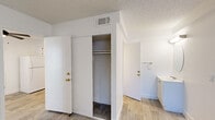 This single-floor unit offers a cohesive, light-filled interior finished in a clean, neutral palette with light wood-look flooring running consistently throughout each room. The layout is practical and well-connected, with rooms flowing naturally from one to the next.

The kitchen is efficiently designed, featuring gray-toned lower cabinetry paired with white upper cabinets, a light stone-look countertop, a geometric tile backsplash, and a black matte faucet over a stainless steel sink. White appliances, including a refrigerator and range, complete the space.

The main living area is open and versatile, benefiting from a ceiling fan with integrated lighting and a window that brings in natural light. A built-in desk with cabinetry offers a dedicated workspace or study area directly within the room.

Bedroom space includes a sliding-door closet with a hanging rod, providing practical storage. The textured ceilings and gold-toned hardware add subtle warmth against the otherwise crisp white walls throughout.

Two bathrooms serve the unit. One features a vanity with an oval mirror and light countertop, while the other includes a tub-shower combination with sliding glass doors and tile surround. Both bathrooms are finished with the same wood-look flooring seen throughout the rest of the space, maintaining a unified aesthetic.