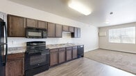 Located at 4551 47th Ave S in Fargo, North Dakota, this studio offers a practical and comfortable single-floor layout designed to maximize every square foot. The open-concept kitchen and living area serves as the heart of the unit, where the kitchen is outfitted with rich dark wood cabinetry, granite-look countertops, and a full suite of black appliances including a refrigerator, range, microwave, and dishwasher. Durable wood-look vinyl flooring runs throughout the kitchen, providing an easy-to-maintain surface that complements the warm cabinetry tones. The living area features plush wall-to-wall carpeting and neutral-toned walls that create a calm, versatile backdrop. A large window floods the space with natural light, while a private exterior door adds both convenience and an airy sense of openness. A carpeted hallway connects the main living space to the two bathrooms, one of which features a walk-in shower with wood-look vinyl flooring. Closet storage is accessible off the hallway, and an electrical panel is neatly recessed into the wall. Throughout the unit, clean white trim, six-panel doors, and baseboard heating contribute to a tidy, functional aesthetic well-suited for everyday living.