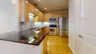 Located at 230 North 6th Street in downtown Richmond, Virginia, Unit 326 is a thoughtfully designed single-floor residence that maximizes its efficient footprint. The open-plan kitchen and living area is anchored by warm hardwood flooring that runs throughout, lending a sense of continuity and brightness to the space. Large windows along one wall flood the living area with abundant natural light, offering views of the surrounding urban streetscape.

The kitchen is well-appointed with light maple cabinetry, a full suite of stainless steel appliances including a range, microwave, and refrigerator, complemented by a subway tile backsplash and dark countertops that provide a striking contrast. A peninsula with bar-height counter space creates a natural division between the kitchen and living area while offering additional workspace. Pendant lighting adds a modern touch overhead.

The entryway is clean and functional, with recessed lighting and crisp white walls establishing an inviting arrival. The bathroom features tile flooring, a maple vanity with granite countertop, a framed mirror, and a full tub-shower combination with subway tile surround and chrome fixtures. The overall aesthetic is modern and clean, with consistent finishes creating a cohesive, urban living environment throughout.
