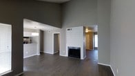 This single-story Dallas property makes a strong architectural impression with its dramatically high ceilings in the main living area, creating an expansive, airy atmosphere. The open-concept layout seamlessly connects the living room to adjacent spaces, enhancing the sense of flow throughout the home. Dark hardwood flooring runs consistently across the main areas, grounding the space with a rich, warm contrast against the neutral gray walls.

The focal point of the living area is a striking fireplace clad in white shiplap, extending nearly floor to ceiling and adding a clean, modern-farmhouse aesthetic. A passthrough or bar area adjacent to the kitchen is visible to one side, accented by a pendant light that hints at a dedicated dining or prep zone nearby. A doorway leads to what appears to be a hallway with access to additional rooms, while a second opening reveals a connecting room with natural light from a window, suggesting versatile use as a bedroom or flex space.

The overall ambiance is modern and understated, with a neutral color palette, clean lines, and thoughtful architectural details that offer a blank canvas ready for personalization.
