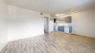 Located at 1469 Zepol Rd in Santa Fe, NM, this single-floor, one-bedroom, two-bathroom unit offers a practical and efficiently designed layout. The open-concept living and kitchen area is the heart of the unit, featuring light-toned vinyl plank flooring throughout and a textured ceiling that adds subtle depth. The kitchen is equipped with gray cabinetry, a white refrigerator, a dishwasher, a sink, and overhead lighting, making it functional and easy to navigate. The living area provides a clean, open canvas with neutral white walls and ample room for furniture arrangement. A window allows natural light to filter in, brightening the space. The bedroom is carpeted for comfort and includes a built-in closet with bifold doors, a window with blinds offering views of the surrounding neighborhood, and direct access to a bathroom featuring a vanity with gray cabinetry and a full tub-shower combination with white tile surround. Two closets throughout the unit offer added storage convenience. The textured ceilings are consistent across rooms, and the overall color palette of whites and light grays gives the unit a clean, cohesive feel. Ceiling-mounted HVAC vents ensure climate control throughout the space.
