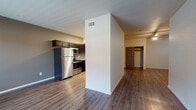 This single-floor unit offers a well-designed open-concept layout that seamlessly connects the living area and kitchen. The kitchen is equipped with a full suite of stainless steel appliances, including a refrigerator, range, microwave, and dishwasher. Rich, dark espresso cabinetry provides generous storage, while granite countertops add a polished, contemporary feel. Wood-look plank flooring runs throughout, providing a cohesive and easy-to-maintain surface across all rooms.

The living area is open and versatile, with neutral-toned walls and recessed lighting that contribute to a bright, welcoming atmosphere. A large window in one of the rooms allows natural light to filter in, offering views of the surrounding exterior. A partial dividing wall between the kitchen and living space adds subtle definition without closing off the floor plan.

The bedroom area, visible through a paneled door, includes closet access, offering practical storage solutions. The bathroom features the same wood-look flooring, a dark vanity with a granite countertop and undermount sink, a mirrored medicine cabinet, and a full bathtub with a shower rod. Clean white walls and recessed lighting keep the bathroom feeling bright and functional. Overall, the unit presents a clean, modern aesthetic with consistent finishes throughout.