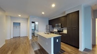 Located at 3443 Park Street in Grove City, Ohio, this single-floor residence offers a thoughtfully designed living space with a clean, modern aesthetic. The kitchen serves as a centerpiece of the home, showcasing sleek dark wood cabinetry that extends floor to ceiling, providing ample storage. A central island with a light stone countertop and an undermount sink adds both functionality and a visual focal point to the space. Stainless steel appliances — including a refrigerator, electric range, and built-in microwave — complete the contemporary kitchen setup. Recessed lighting throughout keeps the space bright and well-illuminated, complementing the light-toned walls that create an open, airy feel. Rich hardwood-style flooring runs throughout, adding warmth and continuity to the space. A dedicated laundry area is conveniently accessible just off the kitchen, housing a full-size washer and dryer. The layout is efficient and well-organized, making thoughtful use of the available floor plan. Overall, the space strikes a balance between modern design and practical functionality, making it a well-appointed residence in Grove City, OH.