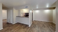 This single-story unit is designed with a functional, open layout that connects the living and kitchen areas seamlessly. Dark wood-style plank flooring runs consistently throughout the main living spaces and bedrooms, providing a cohesive and clean aesthetic against neutral beige walls and white trim.

The kitchen is configured as a galley-style corridor, lined with white cabinetry and dark granite-style countertops. It is equipped with a stainless steel refrigerator and a black range, alongside a double-basin stainless sink. A pass-through counter connects the kitchen to the living area, enhancing the open feel of the space.

The living area is bright and open, receiving natural light through a window, and features a textured ceiling throughout.

Both bedrooms are well-proportioned, each equipped with a ceiling fan with light fixture, wood-style flooring, and windows fitted with blinds that allow for natural light and privacy.

The unit includes two bathrooms. One features a tub-shower combination with full-height earth-toned tile and a decorative mosaic accent border. The second bathroom includes a vanity with dark granite-style countertops, a wide mirror, and overhead lighting.