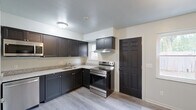 This two-story home in Dayton, Ohio offers a well-organized layout spread across two floors, providing comfortable living with two bedrooms and two full bathrooms. The main floor features a bright living area with durable luxury vinyl plank flooring and a carpeted staircase leading to the upper level. The kitchen is a standout feature, equipped with dark shaker-style cabinetry, granite-look countertops, stainless steel appliances including a range, microwave, and dishwasher, along with a window that brings in natural light and outdoor views. A louvered-door closet adds convenient storage off the kitchen. Both bathrooms are finished in a clean, modern style — one features a white vanity with mirror and a tub/shower combo with light wood-tone LVP flooring, while the other offers a compact vanity setup. The two bedrooms are found on the upper floor, each featuring LVP flooring, neutral painted walls, and windows overlooking the surrounding greenery. The primary bedroom offers a generous footprint. A hallway connects the upper-level rooms, completing the functional two-floor layout of this move-in-ready home.