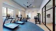 Located at 1201 Callowhill St in Philadelphia's vibrant Callowhill neighborhood, this contemporary fitness center is thoughtfully designed across two dedicated exercise rooms. The main workout area boasts soaring ceilings accented by large industrial-style ceiling fans, creating excellent airflow throughout the space. Expansive windows along the perimeter flood the room with natural light while offering views of the surrounding cityscape, enhancing the overall workout atmosphere.

The primary exercise room is well-appointed with a full suite of cardio equipment, including treadmills, ellipticals, and a rowing machine, all positioned on a blue carpeted zone for comfort and definition. A dedicated strength training area features a comprehensive dumbbell rack, adjustable weight benches, cable machines, and a large wall mirror to aid proper form. Built-in storage cabinetry adds a clean, organized aesthetic.

The secondary exercise room offers a more intimate setting ideal for focused training, housing a stationary spin bike, kettlebells, stability balls, a foam roller, and a wall-mounted smart mirror for guided workouts. Neutral-toned carpeting, crisp white walls, and black-framed glass partition doors tie both rooms together with a sleek, modern design language, making this fitness center a polished and functional amenity.