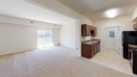 Located on D Avenue in Grand Haven, Michigan, this single-floor unit offers a well-organized layout designed for comfortable everyday living. The open-concept living and dining area is generously proportioned, featuring neutral carpet flooring, crisp white walls, and a sliding glass door that invites abundant natural light and provides views of the surrounding outdoor greenspace.

The galley-style kitchen is efficiently designed with rich dark wood cabinetry lining both sides, granite-look countertops, tile flooring, a double-basin sink, dishwasher, and black appliances including a refrigerator and range. A pass-through connection opens the kitchen toward the main living space, enhancing the overall flow of the unit.

The bedrooms are carpeted and bright, with one featuring dual closets — including a walk-in — alongside direct access to a private en-suite bathroom. Additional bedrooms offer comparable comfort and storage. Both bathrooms are finished consistently, each with dark wood vanities, granite-style countertops, a single sink, tile flooring, and a mirrored vanity. One bathroom includes a tub/shower combination while the other features a standalone walk-in shower. The overall aesthetic throughout is clean, neutral, and move-in ready.