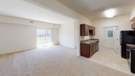 Located on D Avenue in Grand Haven, Michigan, this single-floor unit offers a well-organized layout designed for comfortable everyday living. The open-concept living and dining area is generously proportioned, featuring neutral carpet flooring, crisp white walls, and a sliding glass door that invites abundant natural light and provides views of the surrounding outdoor greenspace.

The galley-style kitchen is efficiently designed with rich dark wood cabinetry lining both sides, granite-look countertops, tile flooring, a double-basin sink, dishwasher, and black appliances including a refrigerator and range. A pass-through connection opens the kitchen toward the main living space, enhancing the overall flow of the unit.

The bedrooms are carpeted and bright, with one featuring dual closets — including a walk-in — alongside direct access to a private en-suite bathroom. Additional bedrooms offer comparable comfort and storage. Both bathrooms are finished consistently, each with dark wood vanities, granite-style countertops, a single sink, tile flooring, and a mirrored vanity. One bathroom includes a tub/shower combination while the other features a standalone walk-in shower. The overall aesthetic throughout is clean, neutral, and move-in ready.