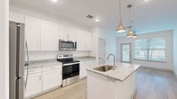 This single-floor residence offers a clean, contemporary design with a bright and airy aesthetic throughout. The kitchen serves as a central highlight, featuring white shaker-style cabinetry, light granite countertops, and a full suite of stainless steel appliances including a range, microwave, and refrigerator. A center island with an undermount sink and pendant lighting above adds both functionality and visual appeal. Light wood-look flooring runs through the main living and kitchen areas, contributing to the home's warm, cohesive feel.

The living area is open and inviting, with natural light streaming in through large windows fitted with blinds, complemented by a ceiling fan. A glass door provides direct access to the outdoors, enhancing the connection between interior and exterior spaces.

The bedrooms are carpeted and comfortably sized, each equipped with ceiling fans and windows that allow for natural light. The rooms offer easy access to adjacent hallways and shared spaces. The bathrooms maintain the design consistency of the rest of the home, featuring white subway-tiled tub-shower combinations, granite-topped vanities with white cabinetry, and wood-look flooring. Overall, the space presents a well-coordinated, move-in-ready interior with modern finishes throughout.