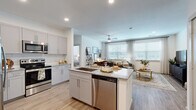 This thoughtfully designed 2-bedroom, 2-bathroom residence offers a seamless open-concept floor plan that maximizes every square foot. The kitchen is a standout feature, showcasing grey shaker-style cabinetry, granite countertops, a subway tile backsplash, stainless steel appliances — including a French door refrigerator and dishwasher — and a central island with a sink, ideal for both meal prep and casual dining. The kitchen flows effortlessly into the living room, which is bathed in natural light from large windows dressed with elegant drapes and blinds, and features a ceiling fan overhead and durable wood-look flooring underfoot. Both bedrooms are generously sized, each offering large windows, ceiling fans, and a calm, neutral palette. The primary bedroom includes its own dedicated closet with wire shelving systems for organized storage. The bathrooms are elegantly finished with marble-style tile surrounds, grey vanities topped with granite countertops, and wood-look flooring that ties the space together. A second bedroom with versatile flex space provides room for a home office setup. Throughout the residence, consistent light-toned flooring, recessed lighting, and a cohesive modern aesthetic create a bright, welcoming atmosphere.