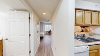 Located at 601 W Cary St in Richmond, Virginia, this compact single-floor unit is thoughtfully designed to maximize every inch of its space. A central hallway connects all areas, creating a logical and efficient flow from entry to living area. The living room serves as the heart of the unit, featuring light-toned wood-look flooring, a ceiling fan, and a large window that invites an abundance of natural light, making the space feel open and airy. A built-in breakfast bar with bar stool seating provides a seamless transition into the kitchen, which is outfitted with warm, honey-toned cabinetry, light countertops, a double-basin sink, and a full suite of white appliances including a dishwasher, electric range, microwave, and refrigerator. The galley-style kitchen layout makes efficient use of the available space. The bathroom features stone-look tile flooring, a wood-toned vanity with a large mirror, a shower-tub combination, and a bright vanity light fixture overhead. Two closets offer convenient storage options throughout the unit, while an in-unit laundry area adds a practical amenity. Crisp white walls and consistent wood-look flooring across the main living areas unify the design, creating a clean and modern aesthetic throughout.