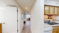 Located at 601 W Cary St in Richmond, Virginia, this compact single-floor unit is thoughtfully designed to maximize every inch of its space. A central hallway connects all areas, creating a logical and efficient flow from entry to living area. The living room serves as the heart of the unit, featuring light-toned wood-look flooring, a ceiling fan, and a large window that invites an abundance of natural light, making the space feel open and airy. A built-in breakfast bar with bar stool seating provides a seamless transition into the kitchen, which is outfitted with warm, honey-toned cabinetry, light countertops, a double-basin sink, and a full suite of white appliances including a dishwasher, electric range, microwave, and refrigerator. The galley-style kitchen layout makes efficient use of the available space. The bathroom features stone-look tile flooring, a wood-toned vanity with a large mirror, a shower-tub combination, and a bright vanity light fixture overhead. Two closets offer convenient storage options throughout the unit, while an in-unit laundry area adds a practical amenity. Crisp white walls and consistent wood-look flooring across the main living areas unify the design, creating a clean and modern aesthetic throughout.