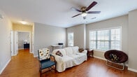 This well-appointed single-story, 1-bedroom, 2-bathroom home in Carrollton, Georgia offers a comfortable and functional layout across a compact, efficiently designed floor plan. The living room is bright and welcoming, featuring warm hardwood flooring, neutral gray walls, a ceiling fan with light fixture, and multiple windows fitted with blinds that allow for abundant natural light and outdoor views. The adjacent dining area continues the hardwood flooring and offers a similarly airy feel, with windows overlooking the outdoors and convenient access to an exterior door. The kitchen is equipped with rich dark-wood cabinetry, light stone-look countertops, and tile flooring, providing ample storage and prep space. The spacious primary bedroom includes a ceiling fan, hardwood floors, and a window that brings in natural light, creating a comfortable retreat. A dedicated laundry room with tile flooring houses a full-size washer and dryer, adding everyday convenience. Two bathrooms, including one with tiled walls, complete the layout. Neutral tones throughout the home lend a cohesive, move-in-ready aesthetic suited for a variety of lifestyles.