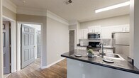 This efficient and thoughtfully designed one-bedroom, one-bathroom residence offers a comfortable and functional layout across a single floor. The living room welcomes you with rich hardwood-style flooring, crown molding, a ceiling fan, and a window that allows natural light to fill the space, creating a warm and inviting atmosphere.

The kitchen is a standout feature, equipped with white shaker-style cabinetry, dark countertops, a subway tile backsplash, and a full suite of stainless steel appliances including a range, over-the-range microwave, refrigerator, and dishwasher. A peninsula with an integrated sink and additional counter space adds both functionality and a natural division between the kitchen and living area.

The bedroom is generously sized, finished with plush carpeting, a ceiling fan with light fixture, and a window overlooking greenery outdoors, providing a peaceful retreat. A dedicated closet offers practical storage. The bathroom features wood-style flooring, a single vanity with dark countertop and large mirror, and a full soaking tub and shower combination. Throughout the unit, neutral tones, clean finishes, and consistent design details contribute to a cohesive and move-in-ready living environment.