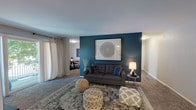 This single-floor residence at Halsey Flats offers a thoughtfully designed layout that balances comfort and modern style. The living room serves as the centerpiece of the space, distinguished by a striking deep teal accent wall that anchors the room and provides a bold contrast to the neutral carpeting and light ceiling. A sliding glass door leads to a private balcony with tree-lined views, filling the space with natural light. The open flow connects the living area to a dedicated dining space, which continues the teal accent wall detail and features a window with natural light — an inviting setting for everyday meals.

The kitchen is equipped with white cabinetry, granite-style countertops, a stainless steel sink, and black appliances, offering a clean and functional workspace. Two bedrooms provide comfortable retreats; one features carpet, a ceiling fan, and a standard window, while the other is a cozier, carpeted room with warm ambient lighting. Throughout the residence, carpet flooring adds warmth, and the consistent use of teal accents lends a cohesive, contemporary aesthetic. The overall ambiance is modern and welcoming, with intentional design details that elevate the everyday living experience.