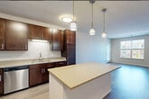 This thoughtfully laid-out one-bedroom, one-bathroom residence offers a comfortable and functional single-floor living experience. The open-concept kitchen and living area serves as the heart of the home, anchored by a central island with a light quartz-style countertop that provides generous prep and dining space. The kitchen is outfitted with rich dark-wood cabinetry, stainless steel appliances including a refrigerator, dishwasher, and range, and a stainless undermount sink. A trio of stylish pendant lights hangs above the island, complementing the flush ceiling fixtures that provide ample illumination throughout. Hardwood-style flooring runs through the kitchen and living areas, lending warmth and a cohesive aesthetic. The living area benefits from natural light through windows with neighborhood views. The bedroom is a well-proportioned retreat finished with plush carpet, a ceiling fan, and a dedicated walk-in closet accessible via a sliding door. The full bathroom features tile flooring, a tub-shower combination, a vanity with dark wood cabinetry, and a large mirror. Neutral tones and clean lines throughout the space create a calm, move-in-ready atmosphere that is both practical and inviting.