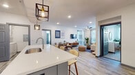 This well-designed single-floor residence offers a thoughtfully planned open-concept layout that seamlessly connects the kitchen, dining, and living areas. The kitchen is a standout feature, showcasing a large island with a shiplap blue accent base, white quartz countertops, gray shaker-style cabinetry, stainless steel appliances, and stylish industrial pendant lighting — a functional and visually striking space for cooking and entertaining. The open living and dining area is bright and airy, benefiting from generous natural light through large windows and sliding glass doors that lead to an outdoor balcony. A ceiling fan and recessed lighting add to the comfortable ambiance, while wood-look flooring runs throughout the main living spaces. The bedrooms are carpeted and well-lit, each featuring large windows that invite ample natural light and views of the surrounding greenery. The primary bathroom offers a sleek walk-in shower with marble-style tile surround and a gray vanity with white quartz countertop, while the secondary bathroom features a full tub-shower combination with similarly refined finishes. Throughout the unit, a cohesive modern aesthetic is maintained with neutral tones, contemporary fixtures, and quality finishes that create a polished and inviting living environment.