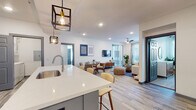 This well-designed single-floor residence offers a thoughtfully planned open-concept layout that seamlessly connects the kitchen, dining, and living areas. The kitchen is a standout feature, showcasing a large island with a shiplap blue accent base, white quartz countertops, gray shaker-style cabinetry, stainless steel appliances, and stylish industrial pendant lighting — a functional and visually striking space for cooking and entertaining. The open living and dining area is bright and airy, benefiting from generous natural light through large windows and sliding glass doors that lead to an outdoor balcony. A ceiling fan and recessed lighting add to the comfortable ambiance, while wood-look flooring runs throughout the main living spaces. The bedrooms are carpeted and well-lit, each featuring large windows that invite ample natural light and views of the surrounding greenery. The primary bathroom offers a sleek walk-in shower with marble-style tile surround and a gray vanity with white quartz countertop, while the secondary bathroom features a full tub-shower combination with similarly refined finishes. Throughout the unit, a cohesive modern aesthetic is maintained with neutral tones, contemporary fixtures, and quality finishes that create a polished and inviting living environment.