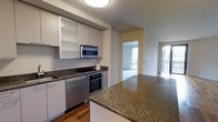 Unit 602 is a well-appointed 1-bedroom, 1-bathroom residence designed with contemporary finishes and a functional open-concept layout. The kitchen serves as a central highlight, featuring rich granite countertops, sleek white cabinetry with frosted glass accents, and a full suite of stainless steel appliances including a built-in oven, microwave, dishwasher, and cooktop. The kitchen island offers additional prep space and creates a natural transition into the living area. Warm hardwood flooring runs throughout, adding a welcoming contrast to the clean, neutral color palette of the walls and cabinetry. The open corridor connects the kitchen seamlessly to the living space, which benefits from large windows that invite generous natural light and offer views of the surrounding cityscape. The overall ambiance is modern and polished, with thoughtful design details that maximize both style and practicality. This single-floor residence presents a cohesive and comfortable living environment well-suited for those seeking a refined urban lifestyle.