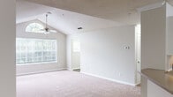 This well-appointed 3-bedroom, 2-bathroom single-story home offers a comfortable and functional layout designed for everyday living. The living room is a standout space, featuring soaring vaulted ceilings with a textured finish, a ceiling fan with light kit, and soft carpeted flooring. Large windows flood the room with natural light, while built-in shelving along one wall adds both character and practicality. The living area flows seamlessly toward the dining area and kitchen, which is highlighted by white cabinetry, a dark electric range, a black refrigerator, a stainless steel sink, and wood-look flooring — a clean, functional galley-style layout. The three bedrooms are carpeted and well-lit with windows offering outdoor views, with the primary bedroom also featuring vaulted ceilings and a ceiling fan. A spacious walk-in closet with wire shelving systems provides generous storage. The two bathrooms are clean and bright, with one featuring a wide vanity with a tan countertop, a large mirror, and wood-look tile flooring. A dedicated laundry area includes a top-load washer and additional wire shelving above for storage. The home is rounded out by a hallway, entrance area, and a second closet, creating a well-organized and livable floor plan throughout.