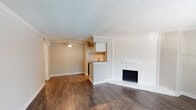 This two-story townhouse in Houston, TX 77058 offers a well-organized layout across two distinct levels. The main floor centers on an open-concept living area finished with rich, dark hardwood-style flooring that runs throughout. A standout feature of the living room is the floor-to-ceiling white-painted brick fireplace, which serves as a striking focal point. Crown molding adds a refined detail along the ceiling line, while a ceiling fan provides practical comfort. The kitchen connects seamlessly to the living space via a peninsula-style breakfast bar with granite countertops, white cabinetry, and black appliances, illuminated by track lighting overhead. Natural light enters through a front-facing window near the entry door, brightening the main living area.

A hallway on the main level leads to a bathroom featuring a granite-topped vanity with an undermount sink and a tiled tub-shower combination. A dedicated laundry closet houses a full-size side-by-side washer and dryer with built-in shelving above.

Upstairs, carpeted flooring provides a softer feel in the bedroom, which benefits from a window view and a ceiling fan. The upper level also includes an additional bathroom with consistent finishes. The overall aesthetic is clean, neutral, and functional throughout.