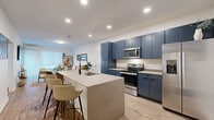 Located at 1599 Oak St in Columbus, Ohio, this thoughtfully designed one-bedroom, one-bathroom residence offers a clean, modern aesthetic throughout its efficiently laid-out single floor. The open-concept kitchen and living area serves as the heart of the home, anchored by a striking kitchen with bold navy-blue cabinetry that extends to the ceiling, providing ample storage. A large quartz-topped island with bar seating and an integrated sink adds both function and style, complemented by a full suite of stainless steel appliances including a refrigerator, range, and microwave. Light wood-tone flooring flows seamlessly throughout, lending warmth and continuity to the space. The living room is bright and inviting, featuring a wall-mounted TV, a glass-panel door that opens to a private outdoor deck, and a wall-mounted mini-split system for climate control. The bedroom is a comfortable retreat with its own mini-split unit, a ceiling fan, and sliding door access with vertical blinds. The bathroom features a floating white vanity, walk-in shower, and clean, contemporary finishes. A hallway and dedicated closet round out the functional layout, making this residence a well-appointed urban home.
