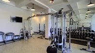Located at 4115 Britton Parkway in Hilliard, Ohio, this fitness center offers a well-appointed, single-floor workout facility designed to support a wide range of training goals. The space features a clean, contemporary aesthetic with a speckled epoxy floor that is both durable and easy to maintain. Structural columns and ceiling beams add architectural definition to the open layout, while industrial-style pendant lighting provides warm, functional illumination throughout.

The strength training area is comprehensively equipped with a multi-station cable machine system, a variety of free weights including dumbbells and kettlebells, adjustable benches, and dedicated weight racks. Full-length mirrors line the walls, enhancing the sense of openness while allowing users to monitor their form during exercises.

The layout is thoughtfully organized to allow ample space for movement between equipment, promoting a comfortable and efficient workout experience. The light-colored walls and reflective mirrors contribute to a bright, energizing atmosphere. Whether focused on functional training, strength building, or general fitness, this facility provides the tools and environment to support an active lifestyle.