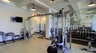 Located at 4115 Britton Parkway in Hilliard, Ohio, this fitness center offers a well-appointed, single-floor workout facility designed to support a wide range of training goals. The space features a clean, contemporary aesthetic with a speckled epoxy floor that is both durable and easy to maintain. Structural columns and ceiling beams add architectural definition to the open layout, while industrial-style pendant lighting provides warm, functional illumination throughout.

The strength training area is comprehensively equipped with a multi-station cable machine system, a variety of free weights including dumbbells and kettlebells, adjustable benches, and dedicated weight racks. Full-length mirrors line the walls, enhancing the sense of openness while allowing users to monitor their form during exercises.

The layout is thoughtfully organized to allow ample space for movement between equipment, promoting a comfortable and efficient workout experience. The light-colored walls and reflective mirrors contribute to a bright, energizing atmosphere. Whether focused on functional training, strength building, or general fitness, this facility provides the tools and environment to support an active lifestyle.