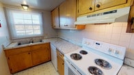 This two-story residence offers 2 bedrooms and 1.5 bathrooms across a well-proportioned floor plan. The kitchen features warm wood cabinetry with ample upper and lower storage, marbled laminate countertops, white appliances including a coil-burner electric range and dishwasher, a tile backsplash, and a double-basin sink positioned beneath a window that allows natural light into the space. A ventilation hood overhead and vinyl tile flooring complete the functional layout.

The living area is generously sized, featuring plush carpeting, neutral walls, and a large sliding glass door fitted with vertical blinds that invite natural light and provide outdoor access. A thermostat and floor vent indicate climate control throughout.

Both bedrooms are carpeted and finished with neutral tones, offering comfortable, quiet spaces. Each room features either a window with blinds or a ceiling-mounted light fixture. The bedrooms provide a calm, functional retreat suitable for a range of furnishing arrangements.

The full bathroom includes a white soaking tub with an overhead shower, fully tiled surround walls, and chrome fixtures, offering a clean and practical design. The overall ambiance of the unit is straightforward and move-in ready.