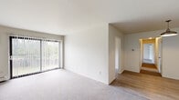 This single-floor unit offers a clean, functional layout with a neutral color palette throughout. The living area is a notable highlight, featuring soft carpeting underfoot and a large sliding glass door dressed with vertical blinds, which allows abundant natural light to fill the room while providing views of the surrounding greenery. A baseboard heating system is present, and the space connects smoothly to additional rooms via an adjoining hallway with wood-look flooring.

The kitchen is efficiently designed with gray cabinetry on both upper and lower sections, white countertops, and a double stainless steel sink positioned beneath a window with vertical blinds. A white electric coil-top range with an overhead exhaust hood completes the cooking area, and the wood-look flooring carries throughout this space.

The bedrooms are carpeted and well-proportioned, each featuring windows with vertical blinds that bring in natural light. One bedroom includes direct access to a full bathroom and a closet, offering added convenience. The bathroom is appointed with a full soaking tub and shower combination, a toilet, vanity, and tile flooring, with baseboard heating rounding out the practical amenities of this straightforward and functional unit.