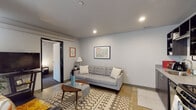 This single-floor unit offers a thoughtfully designed layout that balances functionality with a clean, contemporary aesthetic. The kitchen is equipped with stainless steel appliances, including a range, dishwasher, and over-the-range microwave, complemented by dark cabinetry with open upper shelving and granite-style countertops that provide ample prep space.

The open-plan living and dining area creates a welcoming, versatile space. The dining area accommodates a full table and chairs, while the living zone features recessed lighting and neutral-toned walls that lend a calm, modern atmosphere. A patterned area rug and tufted sofa anchor the living space, which includes wall art and access to adjacent rooms through a sliding barn-style door.

The bedroom is a bright, comfortable retreat highlighted by floor-to-ceiling windows that introduce generous natural light and views of the surrounding exterior. A desk area alongside the windows adds a practical workspace element.

The full bathroom includes a tub-shower combination with a curtain, a vanity with granite-style countertops featuring dark wood cabinetry, and neutral tile flooring. Throughout the unit, recessed lighting, clean lines, and a cohesive neutral palette contribute to a modern, well-organized living environment.