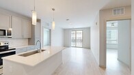 Located at 10747 S Havana St in Lone Tree, Colorado, this two-bedroom, two-bathroom residence offers a thoughtfully designed single-floor layout with a clean, modern aesthetic throughout. Light wood-tone flooring runs continuously across the living areas, complementing the bright white walls and creating a cohesive, airy atmosphere.

The kitchen serves as a central hub of the home, featuring a large island with an undermount sink, quartz countertops, subway tile backsplash, gray shaker-style cabinetry, and stainless steel appliances including a side-by-side refrigerator with ice dispenser, electric range, and microwave. Pendant lighting above the island adds a contemporary touch. The kitchen opens directly to the living area, which benefits from natural light and access to a private balcony through sliding glass doors.

The primary bedroom offers a comfortable footprint with a ceiling fan and a dedicated walk-in closet featuring full-length hanging rods. The second bedroom also includes its own closet with built-in rod storage. Both bathrooms are finished with quartz vanities, gray cabinetry, and tiled tub-shower combinations. An in-unit stacked washer and dryer is also included within the layout.
