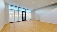 Located at 5395 Martway St in Mission, Kansas, this contemporary two-story unit offers a thoughtfully designed layout across two well-proportioned floors. The main level features a spacious living room distinguished by dramatic floor-to-ceiling windows with sleek black frames, flooding the space with natural light and offering open views of the surrounding streetscape. Light-toned hardwood flooring runs throughout, complementing the clean white walls and recessed lighting overhead.

The upper level houses the private bedroom, which features a large picture window with a ceiling fan, continuing the modern aesthetic with the same warm wood flooring. An adjacent closet with a built-in rod provides convenient storage. The loft-style interior design element adds visual interest with split-level wall detailing.

Two well-appointed bathrooms serve the unit. One features a floating white vanity with an integrated sink and large mirror, while the second offers a full bathtub and shower combination alongside a white cabinetry vanity. Both maintain a crisp, minimalist style consistent with the rest of the unit.

Two staircases connect the floors, enhancing accessibility and flow. The overall design is clean, modern, and light-filled, making this a bright and functional space in the heart of Mission, KS.