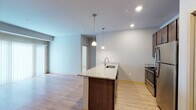 Located at 7944 Watts Rd in Madison, Wisconsin, this single-floor unit offers a well-designed, contemporary layout with a clean, neutral palette throughout. The open-concept kitchen and living area serves as the heart of the space, anchored by a granite-topped center island with a built-in sink and pendant lighting overhead. Dark-toned cabinetry contrasts elegantly with the light granite countertops, while stainless steel appliances — including a refrigerator and range — add a modern, functional touch. A pantry closet with bifold doors provides ample storage. Light hardwood-style flooring runs throughout the main living and kitchen areas, contributing to a bright, airy atmosphere. The living area benefits from a sliding glass door that invites natural light and outdoor access. The bedrooms feature plush carpet, ceiling fans, and generous closet space, including a walk-in closet outfitted with wire shelving systems. Two full bathrooms mirror each other in design, each featuring a dark vanity with white countertop, a large wall mirror with overhead lighting, tile flooring, and a shower-tub combination. The unit's consistent finishes and thoughtful layout make it a practical and attractive space.