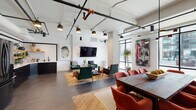 The clubhouse at 5126 Peachtree Blvd in Chamblee, GA, is a thoughtfully designed community space that blends industrial aesthetics with modern comfort. The open-concept main floor is anchored by soaring ceilings with exposed black piping, track lighting, and large floor-to-ceiling black-framed windows that flood the interior with natural light and offer views of the surrounding streetscape.

The lounge area features rich emerald green velvet armchairs, a marble-topped coffee table, layered area rugs over warm hardwood flooring, and curated wall art — creating an inviting, gallery-like atmosphere. Adjacent to the lounge, a formal dining zone offers a substantial dark wood table surrounded by terracotta-hued upholstered chairs, set against a striking textured stone accent wall.

The kitchen area is equipped with black cabinetry, white countertops, open wood shelving styled with decorative accents, geometric tile backsplash, and a full-size black refrigerator — making it well-suited for gatherings and events.

A separate, more intimate conference or meeting room provides a focused setting with polished concrete floors, chalkboard walls framed in wood, a natural wood communal table, and a wall-mounted display screen — ideal for presentations or collaborative work sessions.

The entry corridor features textured stone walls, large-format dark tile flooring, and glass-paneled doors, providing a welcoming and polished arrival experience throughout.