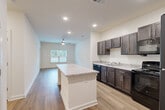 This 2-bedroom, 1-bathroom residence is thoughtfully laid out across a single floor, offering a clean, modern aesthetic with consistent finishes throughout. The open-concept kitchen and living area serves as the heart of the home, anchored by a large center island with granite-look countertops that provides both prep space and casual seating. The kitchen features dark espresso cabinetry, black appliances including a refrigerator, range, and dishwasher, complemented by warm wood-look flooring that extends into the living area. A ceiling fan and a window overlooking greenery bring light and airflow into the living space. The primary bedroom is generously sized, carpeted for comfort, and equipped with its own ceiling fan. It connects directly to a walk-in closet outfitted with multi-tier wire shelving for organized storage. The second bedroom is also carpeted and features its own dedicated closet with wire shelving. The full bathroom includes a granite-top vanity with dark wood cabinetry, a mirror, and a tub-shower combination with brushed nickel fixtures. Throughout the residence, neutral tones and clean lines create a bright, move-in-ready environment suited for modern living.