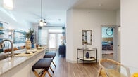 This single-floor residence showcases a thoughtfully designed open-concept layout that seamlessly connects the kitchen, dining, and living areas. The kitchen is equipped with gray shaker-style cabinetry, granite countertops, a subway tile backsplash, stainless steel appliances, and a peninsula island with an undermount sink and pendant lighting overhead — offering both functionality and style. Wood-look plank flooring flows throughout the main living areas, adding warmth and cohesion.

The living room is bright and inviting, featuring large windows with blinds and floor-to-ceiling drapes that invite abundant natural light. A ceiling fan adds practicality, while a glass-paned exterior door enhances the airy feel of the space. A dedicated entryway area with a console table provides a welcoming transition into the home.

The bedroom is a comfortable retreat with plush wall-to-wall carpeting, a ceiling fan, and a generously sized window dressed with teal drapes that filter soft natural light. The bathroom features a granite-topped vanity with ample storage, tile flooring, and a combined soaking tub and shower with tiled surround. Clean white walls and bright lighting complete the polished, modern aesthetic throughout.