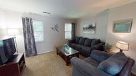 Located at 1910 N Scarlet Maple Ln in Elkhart, Indiana, this single-story home offers a well-organized layout designed for comfortable everyday living. The living room serves as the central gathering space, featuring wall-to-wall carpeting, crown molding, and multiple windows dressed with patterned curtains that invite natural light while maintaining privacy. The room provides ample space for seating arrangements and entertainment.

The kitchen is equipped with warm-toned wood cabinetry offering generous storage, light-colored countertops, and a full suite of black appliances including a refrigerator, range, built-in microwave, and dishwasher. A range hood is mounted above the stove, and recessed lighting illuminates the space. Light-toned flooring completes the functional design.

The home includes multiple bedrooms, each finished with soft carpeting and windows providing natural light. The rooms offer sufficient space for standard bedroom furnishings and feature neutral wall tones throughout.

The bathroom includes a tub and shower combination with tiled surrounds, a single-sink vanity with storage below, and light flooring. The overall design of the home maintains a consistent, neutral palette, creating a cohesive and practical living environment throughout.