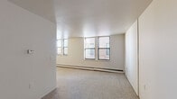 This 2-bedroom, 1-bathroom unit in Detroit, MI (48202) offers a functional and straightforward layout across a single floor. The spacious primary bedroom is notably generous in size, featuring neutral carpet flooring, crisp white walls, and multiple windows that allow for ample natural light and views of the surrounding brick exterior. Baseboard heating runs along the walls, providing efficient climate control throughout the space. The second bedroom is more compact but equally bright, with a window overlooking the exterior and the same carpeted flooring and baseboard heating found throughout the unit. The entry area provides access to the main living spaces and features warm-toned wooden interior doors, adding a touch of classic character. The kitchen is efficiently designed with wood-toned cabinetry and is partially separated from the living area by a dividing wall, creating a defined cooking space. The bathroom is clean and functional, featuring a full tiled tub-shower combination with classic white subway tile surround, a window with exterior views, and a baseboard heater. Overall, the unit maintains a clean, simple aesthetic with neutral tones throughout, making it a practical and adaptable living space in the heart of Detroit.