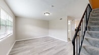 This two-floor space is designed with a clean, neutral aesthetic throughout, offering a cohesive and functional layout. The main level greets visitors with light wood-style luxury vinyl flooring that extends through the open living area and into the kitchen. A staircase with a black metal railing leads to the upper floor, while a large window allows natural light to fill the entry area.

The kitchen is well-appointed with white shaker-style cabinetry, dark granite countertops, a mosaic tile backsplash, and a full suite of stainless steel appliances, including a gas range, microwave, and dishwasher. Light wood-style flooring continues here, complementing the crisp cabinetry.

Upstairs, a hallway with matching flooring connects the bedrooms and bathroom. The bedrooms feature neutral carpet, ceiling fans with light fixtures, windows with blinds, and closets. One bedroom provides direct access to the bathroom, offering added convenience.

The bathroom includes a white vanity with a large mirror, brushed nickel fixtures, and a tub-shower combination surrounded by marble-style tile, with a window for natural ventilation. The overall palette of warm whites and soft grays gives the entire space a consistent, move-in-ready feel.