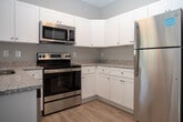 Located at 1715 Sherwood St in Greensboro, NC, this single-floor residence offers a well-designed layout with modern finishes and a bright, welcoming atmosphere throughout. Light-toned hardwood-style flooring flows seamlessly across the main living areas, creating a cohesive and clean aesthetic.

The kitchen is a standout feature, showcasing white shaker-style cabinetry, granite countertops, and a full suite of stainless steel appliances, including a range, microwave, dishwasher, and refrigerator. A peninsula with pendant lighting above provides additional counter space and serves as a natural transition into the living area, making it ideal for both everyday use and entertaining.

The living and bedroom spaces are finished with the same warm flooring and neutral wall tones, complemented by large windows fitted with blinds that allow abundant natural light while maintaining privacy. Views of surrounding greenery add a serene quality to the interior.

The bathroom is appointed with marble-look tile flooring, a granite-topped vanity with white cabinetry, and a tub-shower combination, all contributing to a clean and polished finish. Throughout the residence, white panel doors, recessed lighting, and consistent neutral tones unify the space with a modern yet understated design sensibility.